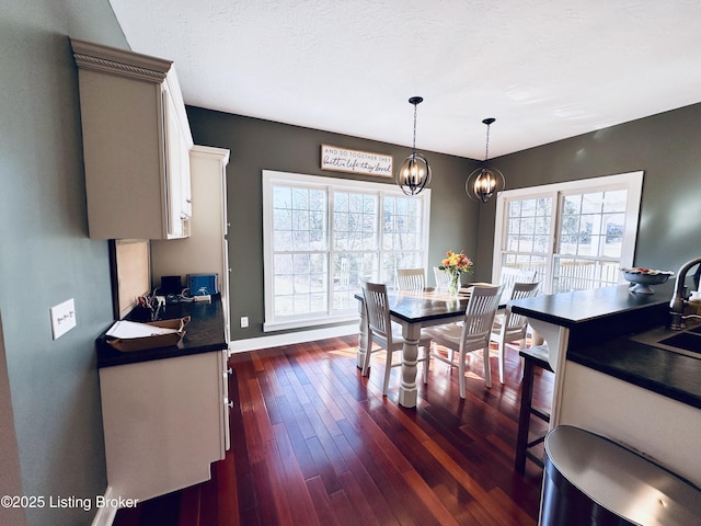 dining area featuring dark wood-style floors, a chandelier, a textured ceiling, and baseboards