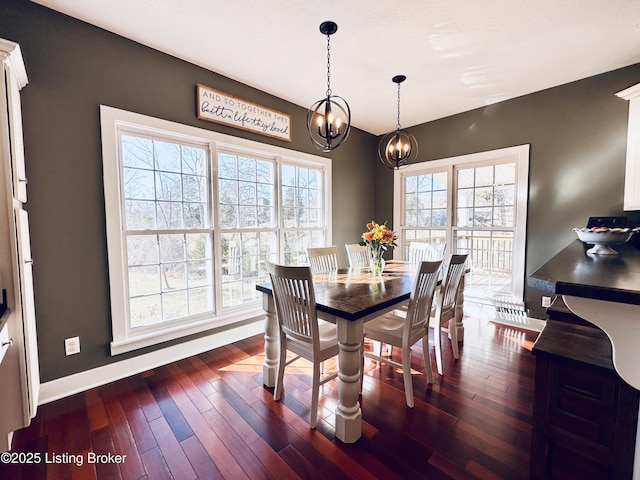 dining area with dark wood-style floors, a notable chandelier, and baseboards