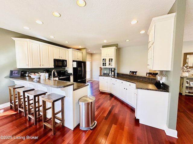 kitchen with dark wood-style floors, a breakfast bar, dark countertops, a peninsula, and black appliances