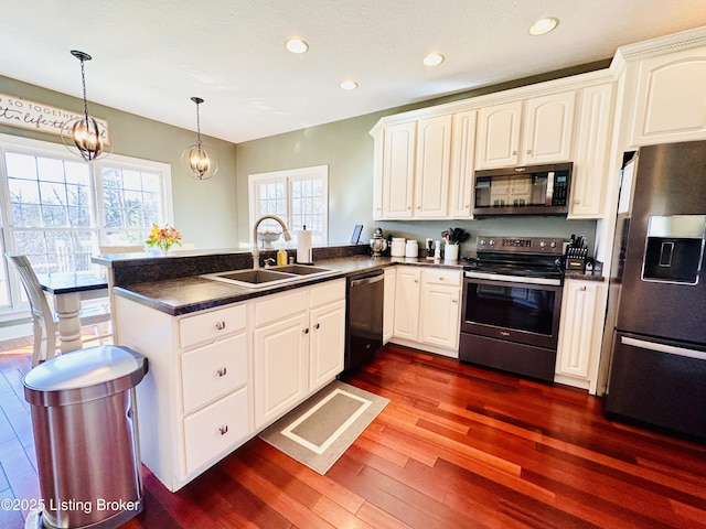 kitchen with dark wood-style flooring, dark countertops, appliances with stainless steel finishes, a sink, and a peninsula