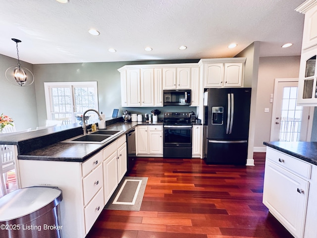 kitchen featuring dark countertops, black appliances, a peninsula, and a sink