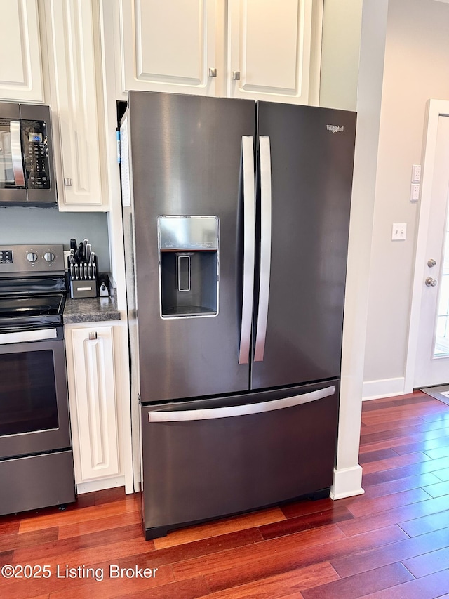 kitchen with stainless steel appliances, white cabinetry, dark wood finished floors, and baseboards