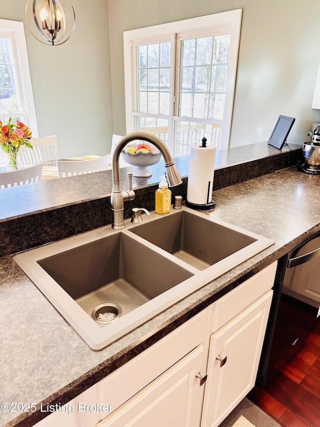 kitchen with dark countertops, black dishwasher, white cabinets, and a sink