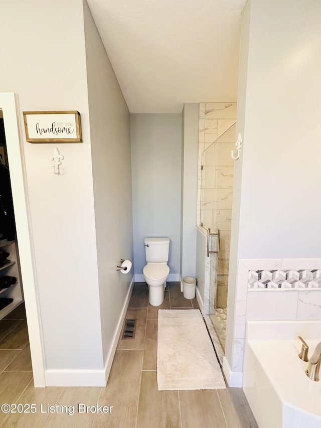 bathroom with a garden tub, toilet, visible vents, baseboards, and a shower stall