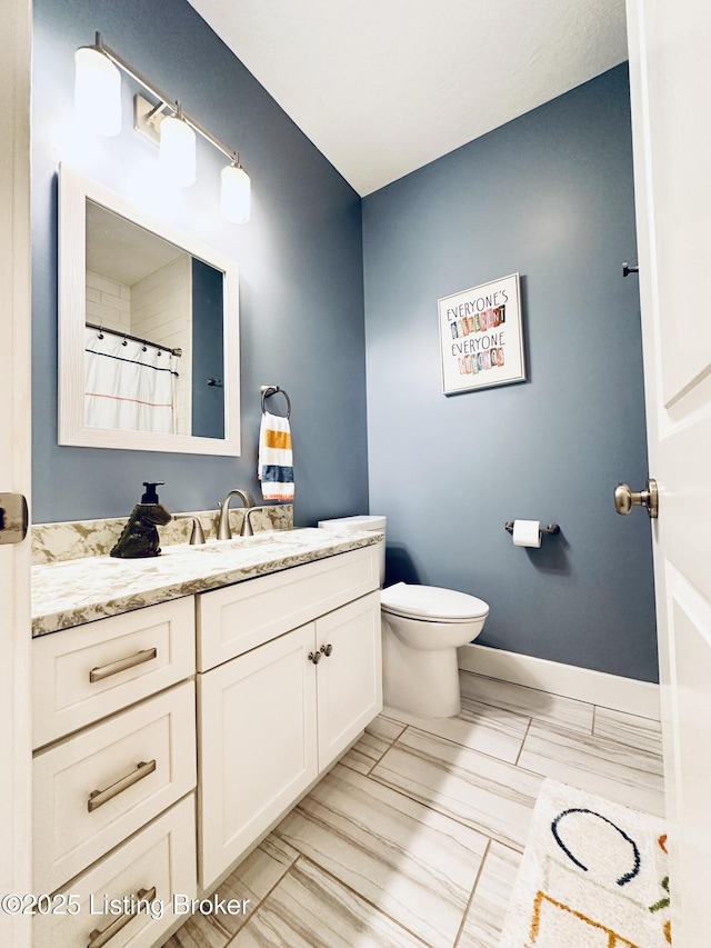 full bathroom with toilet, vanity, and baseboards