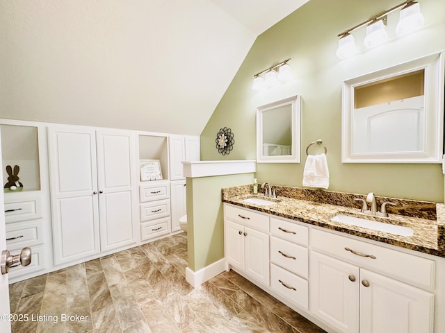 full bath with double vanity, toilet, vaulted ceiling, and a sink