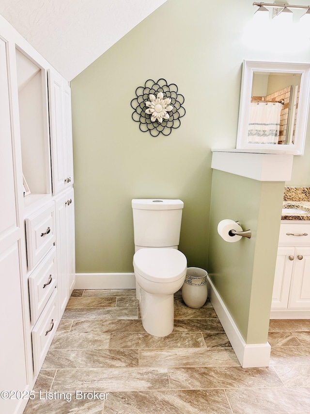 full bathroom featuring baseboards, vaulted ceiling, vanity, and toilet