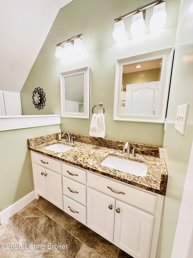 full bathroom featuring vaulted ceiling, a sink, baseboards, and double vanity