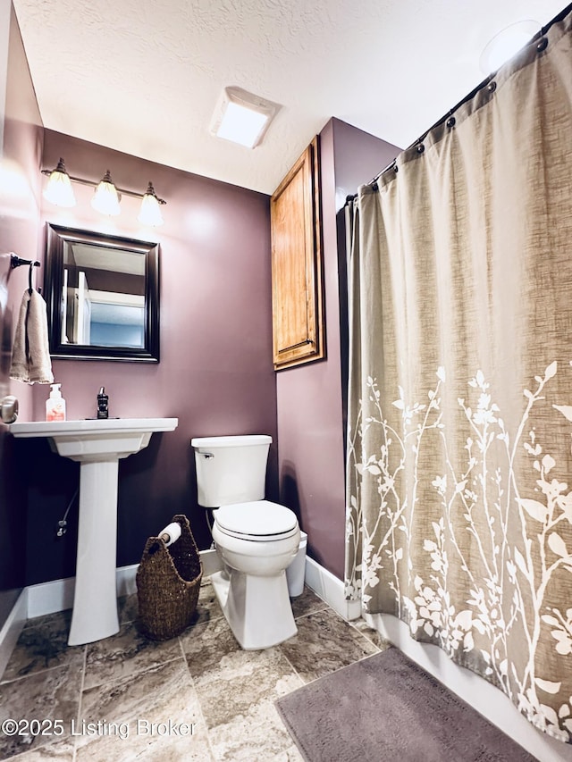 bathroom with a textured ceiling, shower / bath combo, toilet, and baseboards