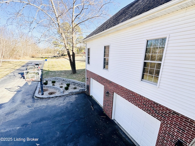 view of property exterior with a garage, brick siding, driveway, and roof with shingles