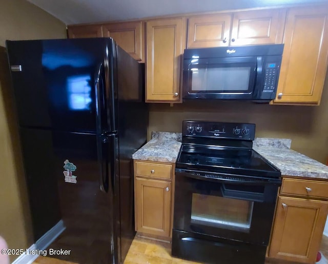 kitchen with light stone counters, black appliances, and brown cabinetry