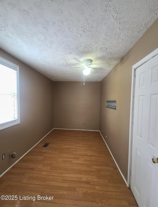 spare room with a ceiling fan, baseboards, wood finished floors, visible vents, and a textured ceiling