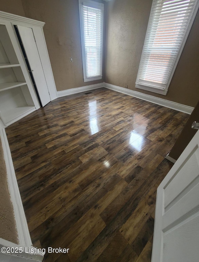 unfurnished bedroom with dark wood-style floors, baseboards, and a textured wall