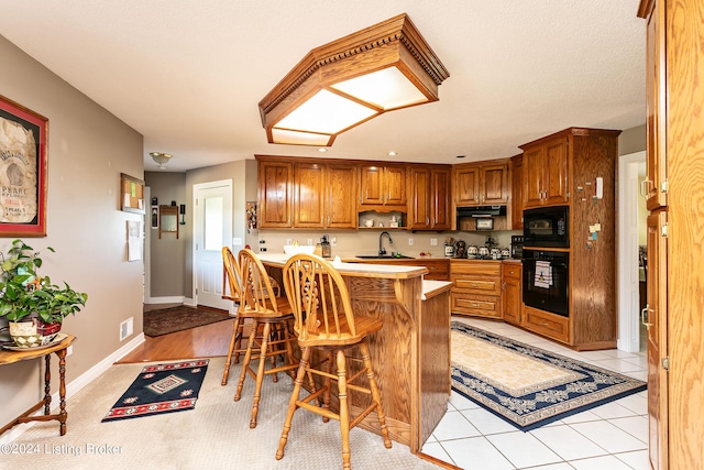 kitchen with brown cabinets, light tile patterned floors, a sink, black appliances, and a kitchen breakfast bar