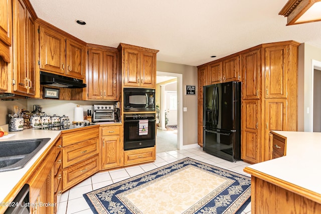 kitchen with light tile patterned floors, light countertops, a sink, under cabinet range hood, and black appliances