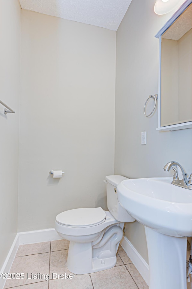 half bath with toilet, tile patterned flooring, baseboards, and a textured ceiling