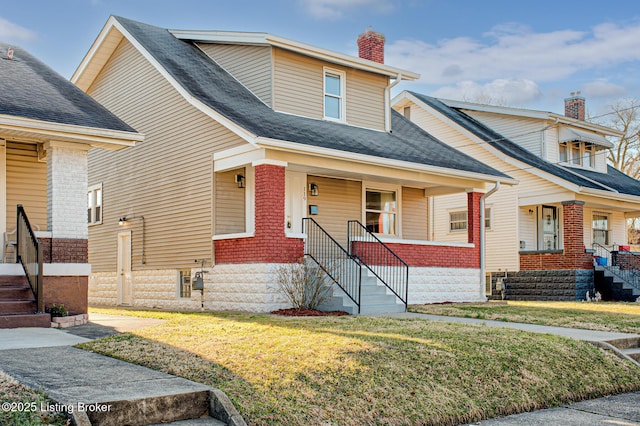 view of front of home with a front lawn, a chimney, a porch, and brick siding