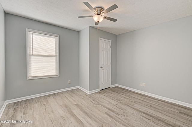 empty room with ceiling fan, a textured ceiling, baseboards, and wood finished floors