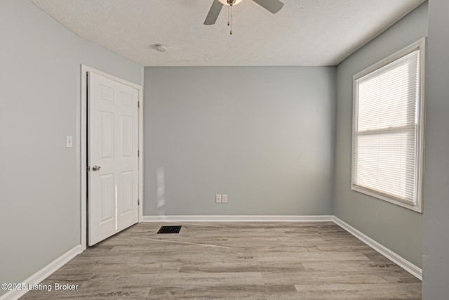 spare room with a textured ceiling, ceiling fan, visible vents, baseboards, and light wood finished floors