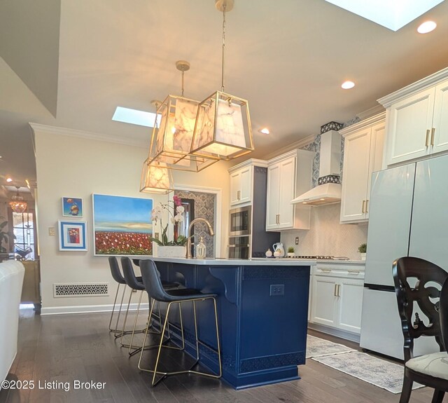 kitchen featuring wall chimney range hood, a skylight, a center island with sink, and freestanding refrigerator