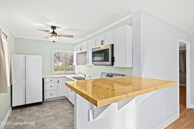 kitchen with stainless steel microwave, a sink, freestanding refrigerator, and white cabinetry