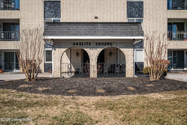 property entrance featuring brick siding, mansard roof, and roof with shingles