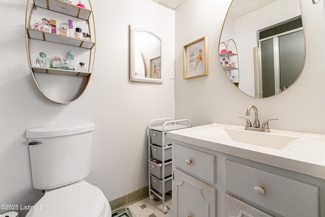 bathroom featuring tile patterned flooring, toilet, vanity, baseboards, and a shower with door