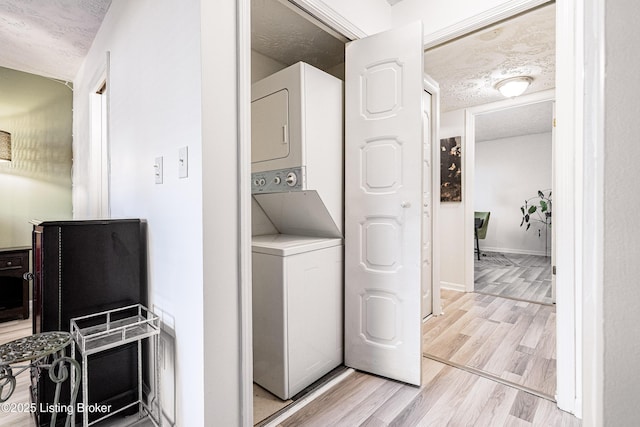 washroom featuring a textured ceiling, stacked washer and dryer, laundry area, baseboards, and light wood finished floors