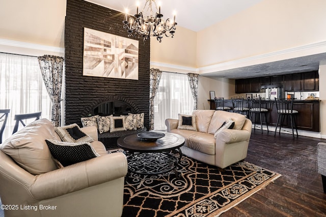 living area featuring a towering ceiling, a brick fireplace, a chandelier, and dark wood-type flooring