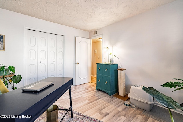 office area with light wood-style flooring, visible vents, and a textured ceiling