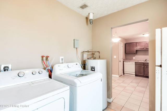 washroom featuring a textured ceiling, light tile patterned floors, separate washer and dryer, a sink, and visible vents