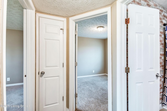 hall featuring carpet, baseboards, and a textured ceiling