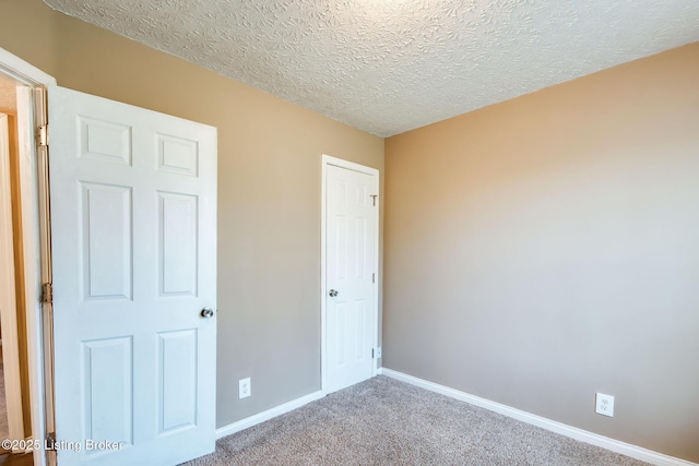 unfurnished bedroom with carpet, a textured ceiling, and baseboards