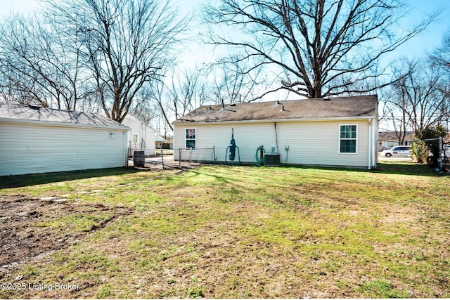 rear view of house with central AC, a lawn, and fence