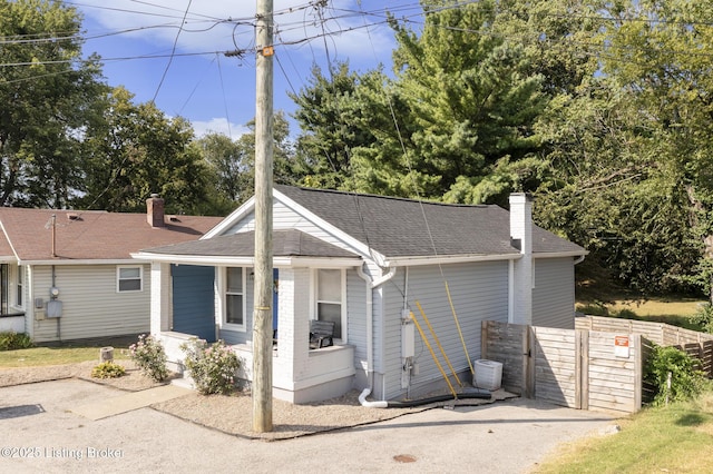 single story home featuring roof with shingles, a chimney, a porch, fence, and cooling unit