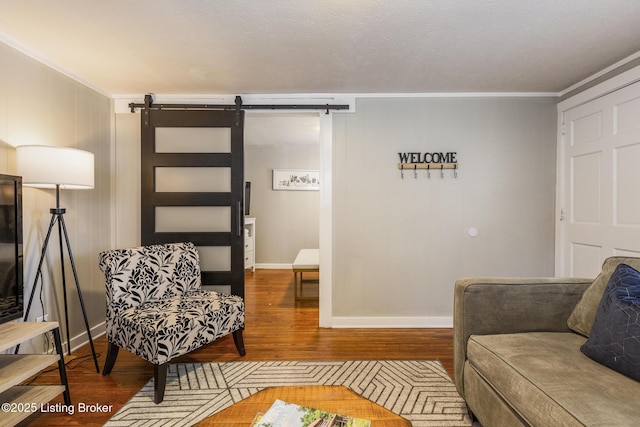 living room featuring wood finished floors, crown molding, baseboards, and a barn door