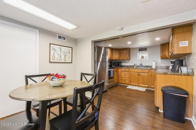 kitchen with brown cabinetry, dark countertops, dark wood-style floors, appliances with stainless steel finishes, and a textured ceiling