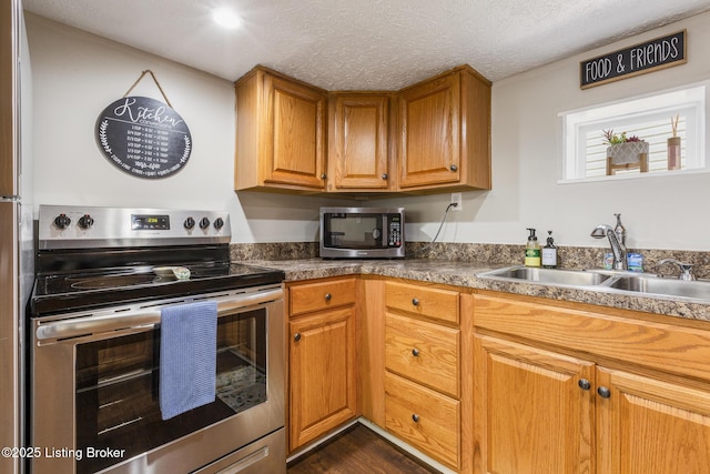 kitchen with a textured ceiling, stainless steel appliances, a sink, and brown cabinets