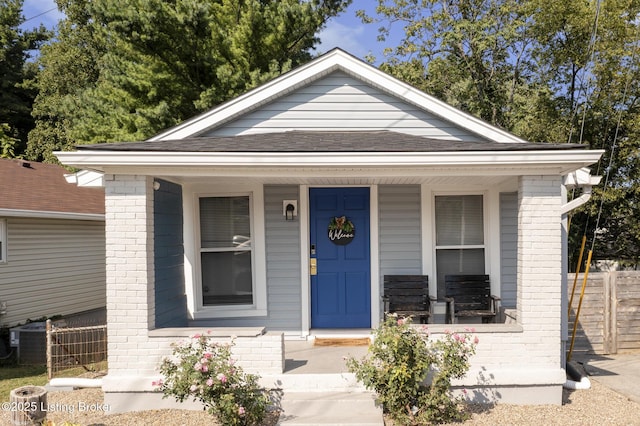 view of front of property featuring a shingled roof, covered porch, brick siding, and fence