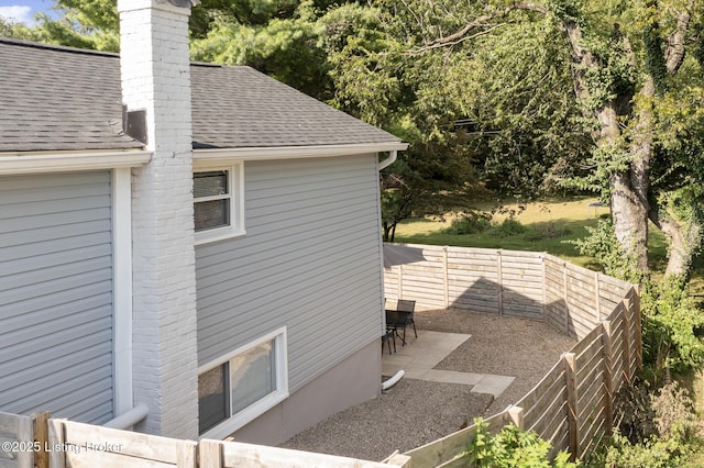 view of home's exterior with a shingled roof, a fenced backyard, and a chimney