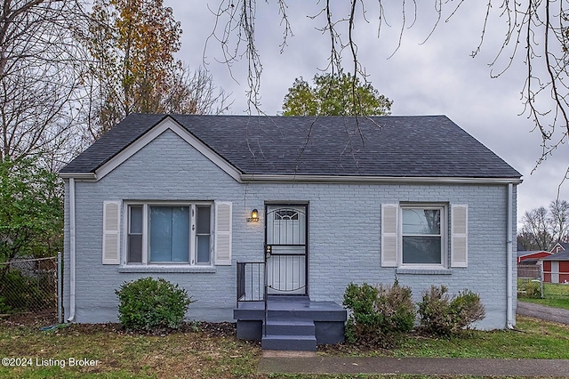 view of front facade featuring roof with shingles, fence, and brick siding