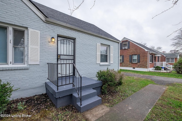 doorway to property with a shingled roof and brick siding