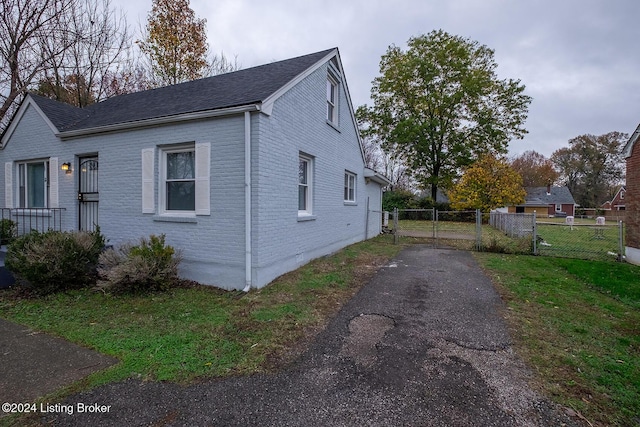 view of side of property with driveway, a gate, fence, and brick siding