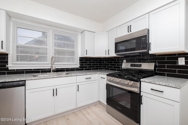 kitchen with appliances with stainless steel finishes, white cabinets, a sink, and decorative backsplash