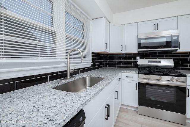 kitchen with white cabinets, decorative backsplash, light stone countertops, stainless steel appliances, and a sink