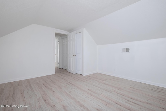 bonus room featuring light wood-style floors, baseboards, visible vents, and vaulted ceiling