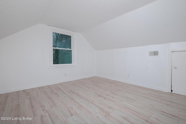 additional living space with baseboards, visible vents, vaulted ceiling, and light wood finished floors