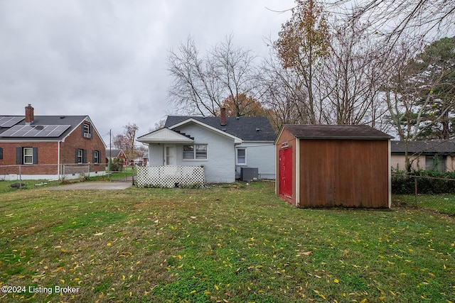 back of property featuring an outbuilding, central AC unit, a fenced backyard, a yard, and a storage unit