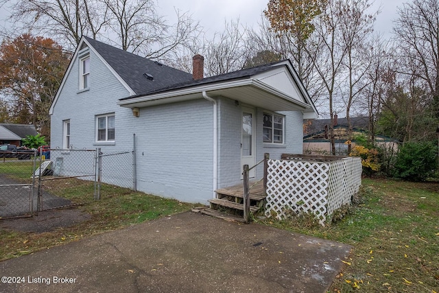 exterior space with a shingled roof, a chimney, a gate, fence, and brick siding