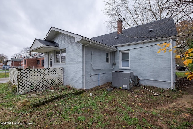 rear view of house featuring roof with shingles, a chimney, central AC, and brick siding